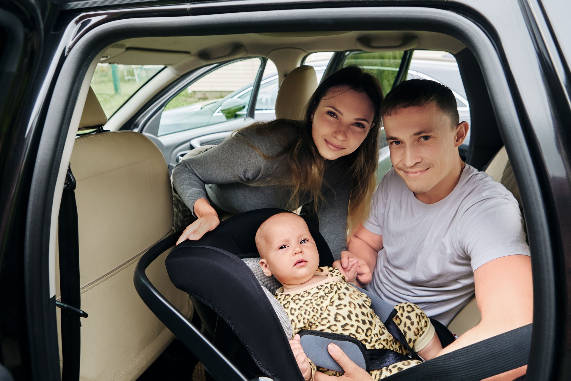 Young parents place baby in rear facing child car seat and tightening safety harness strap.